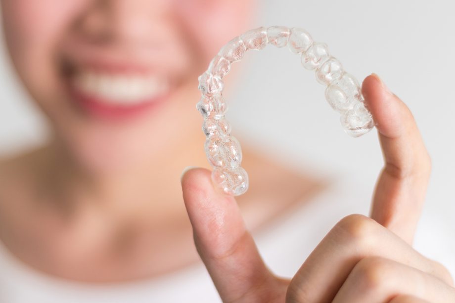 smiling patient holds an Invisalign clear aligner tray