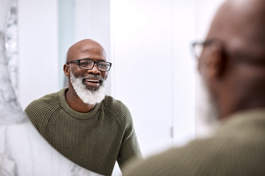a bearded man smiles at himself in a mirror