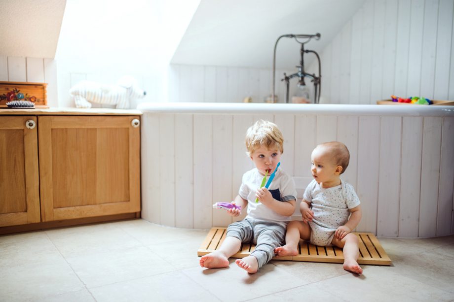 two children with toothbrushes sit by bathtup
