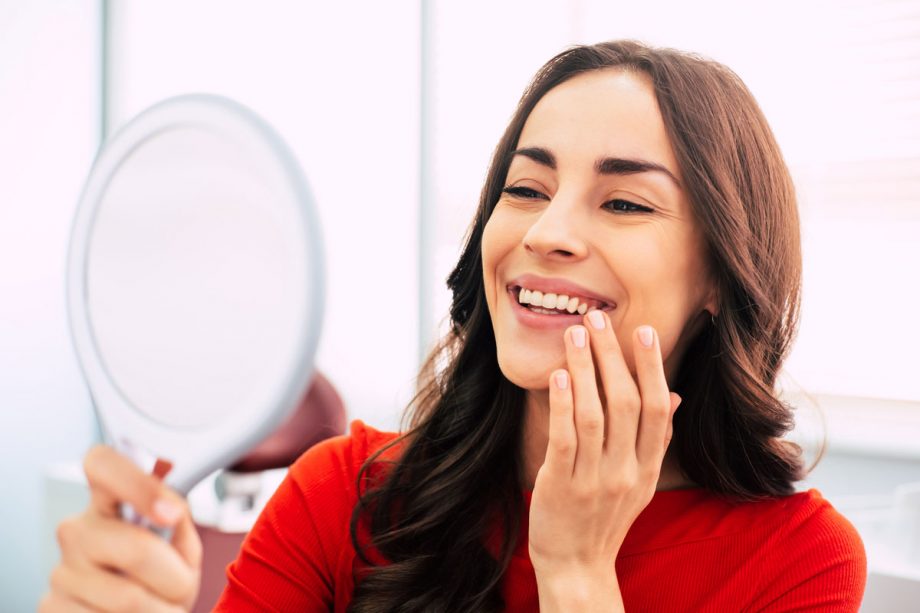 a woman smiles into a hand mirror